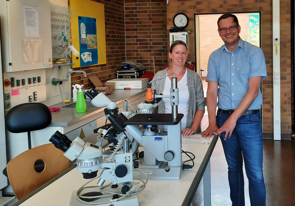 Die Spenderin Jennifer Celner mit Schulleiter Timo Lichtenthäler hinter den gespendeten Mikroskopen 